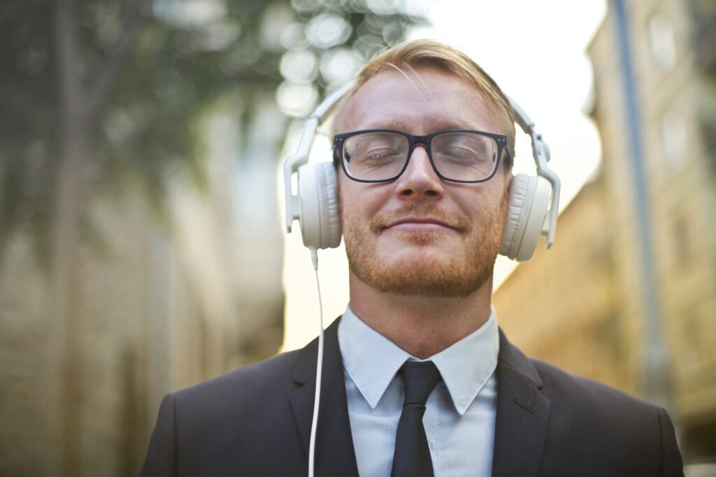A man in a suit prioritizing himself, listening to music through his headphones with his eyes closed.