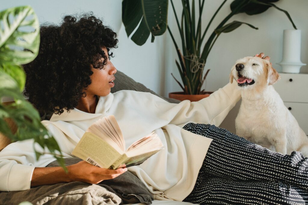 A young Black woman reading and petting her dog on her day off.