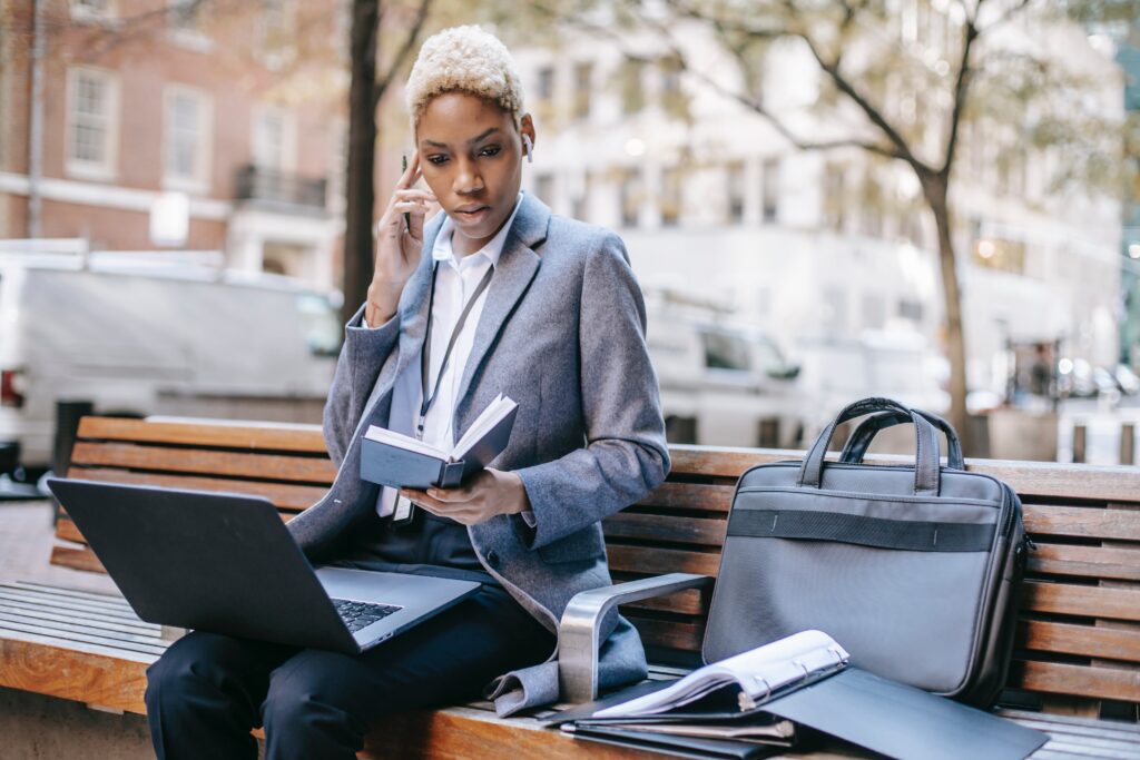 A Black businesswoman multitasking on a park bench