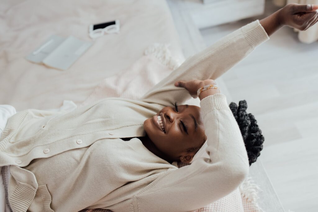 A Black woman, who decided to take a break, smiling and hanging off her bed.