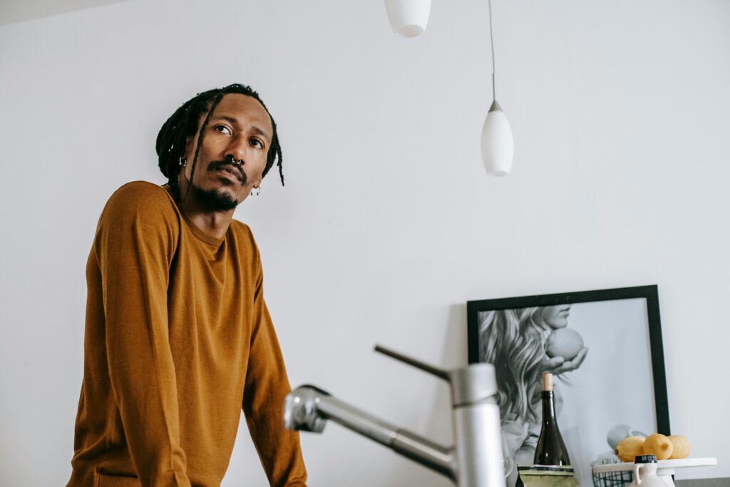 A Black man taking some alone time, standing in his kitchen.