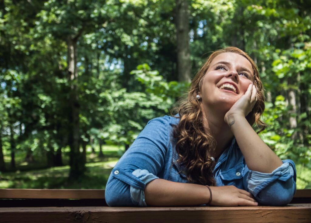 A young white woman smiling in nature after having a change of perspective.