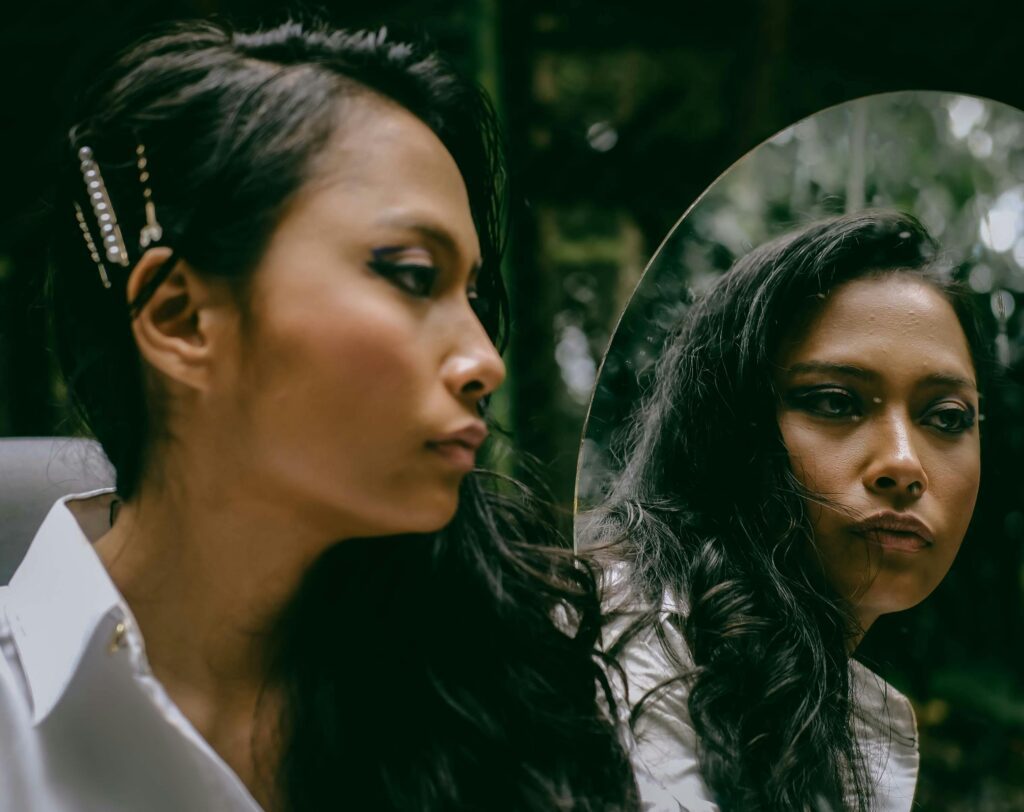 Check in with yourself | A woman mentally reflects beside a mirror.